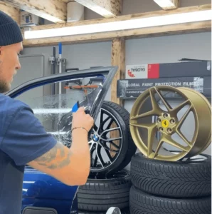 Stagiaire appliquant un film solaire noir sur un vitrage automobile.