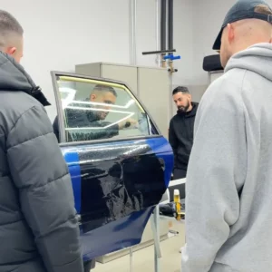 Un stagiaire effectue une découpe de précision sur un film teinté posé sur une vitre latérale.