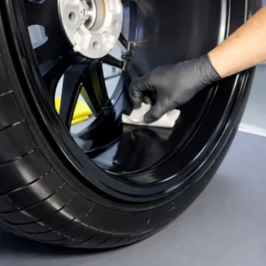 Application d'un traitement céramique sur une jante noire brillante avec gant.
