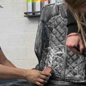 Nettoyage en profondeur d'un siège auto en cuir noir avec brosse et mousse.