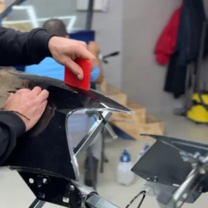 Main experte utilisant une raclette pour finaliser la pose d'un film PPF.